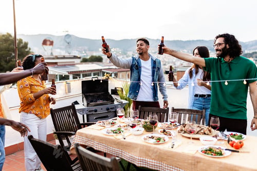 Preview: Young group of friends cheering with beer at terrace party.