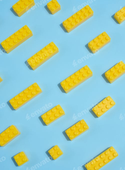 Preview: Scattered yellow plastic toy building bricks on a blue background.