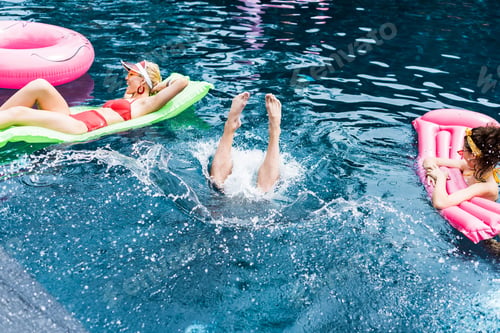 Preview: male legs sticking out from water between two female friends on inflatable mattresses in swimming