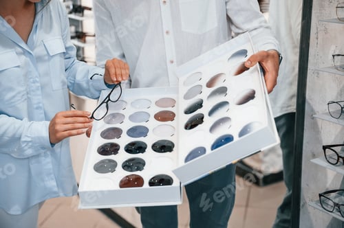 Preview: Bunch of replaceble lenses. Man and woman in the glasses store. Helping to choose product
