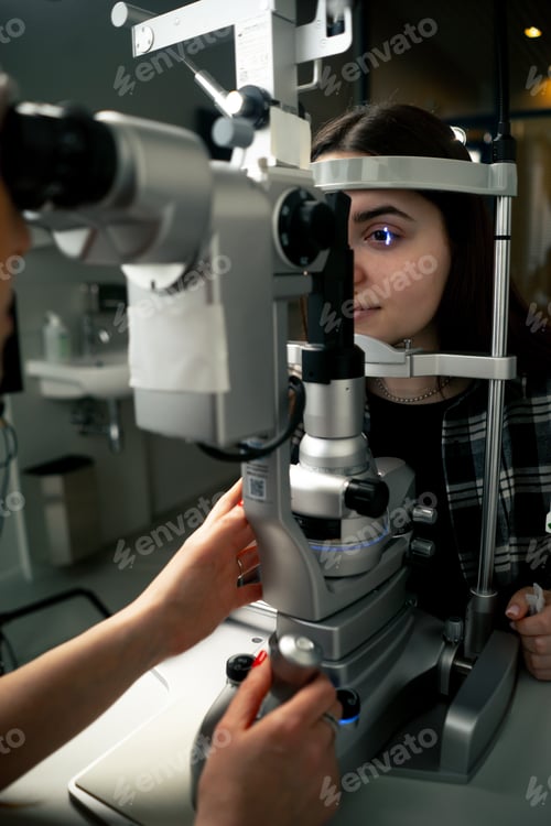 Preview: in an ophthalmology clinic young doctor diagnoses a young girl with a magnifying lens