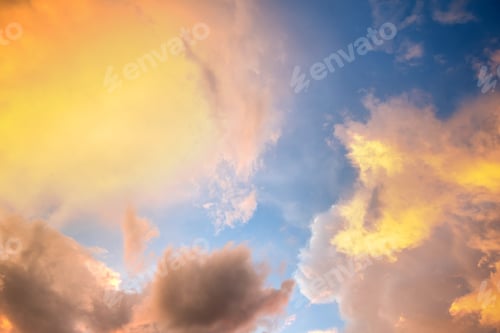 Preview: Dramatic cloudy sunset landscape with puffy clouds lit by orange setting sun and blue sky.