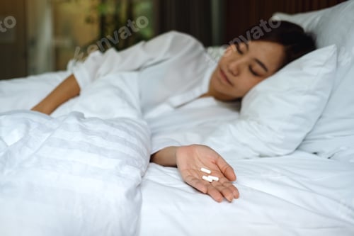 Preview: Closeup image of a sick woman sleeping and lying down on a bed with white pills in hand