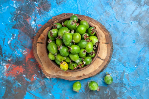 Preview: Above view of delicious vitamin bomb fresh feijoas in a brown pot on wooden tray on blue background