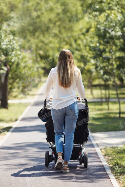 Preview: Young mom from back walking with twin baby stroller in green spring city park.