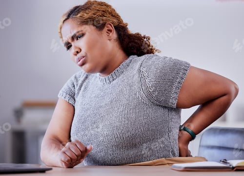 Preview: Corporate employee suffering from back pain while working at a desk in an office, uncomfortable and