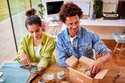 Preview: Young Couple Running Online Business From Home Packing Boutique Candles Ready For Shipping