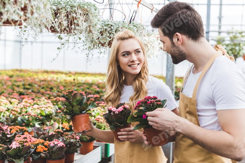 Preview: Smiling gardeners holding pots with flowers in greenhouse