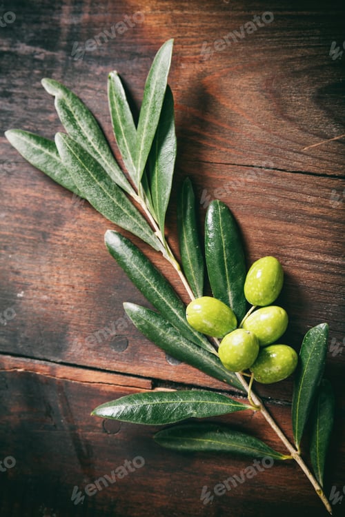Preview: Olive tree twig with raw green olives on wood. Closeup vertical top view.