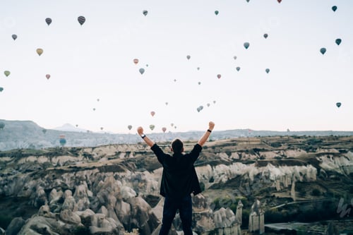Preview: Faceless motivated man raising arms up against hot air balloons