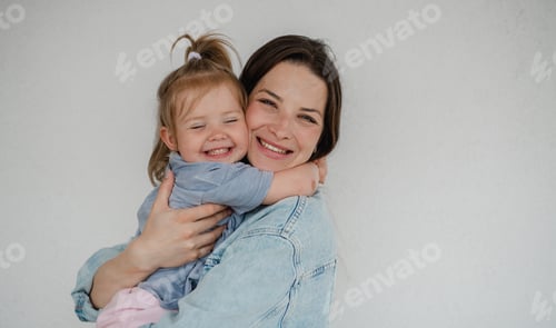 Preview: Happy young mother with her little daughter hugging and looking at camera, on white background.