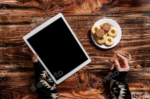 Preview: Woman's hands holding digital tablet and eating cookies on the wooden table
