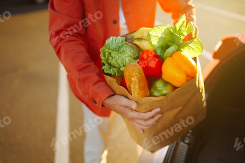 Preview: Healthy vegan vegetarian food in a paper bag in the male hands. Man with shopping bag near the car.