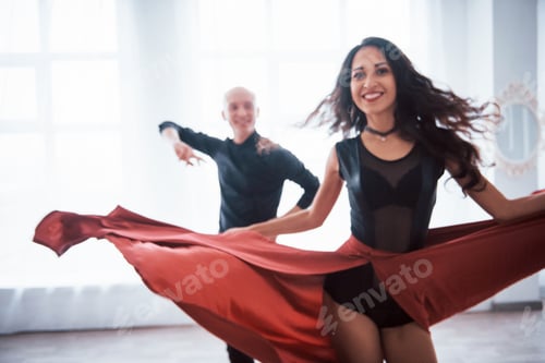 Preview: Young pretty woman in red and black clothes dancing with bald guy in the white room
