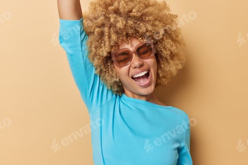 Preview: Happy carefree European woman with curly hair dances and moves carefree exclaims from joy wears sung