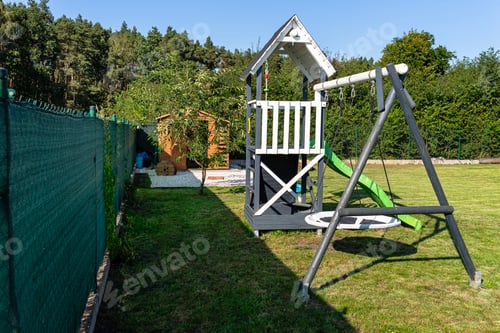 Preview: A childrens playground made of wood and painted white and navy blue, standing in the garden.