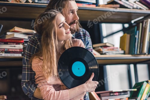 Preview: Beautiful young couple standing embracing and holding vinyl record
