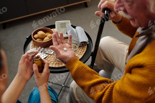 Preview: Senior Caucasian Man Holding Pills While Receiving Assistance from Caregiver