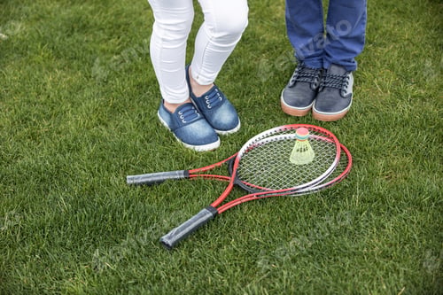 Preview: cropped view of children standing near badminton racquets and shuttlecock on green grass