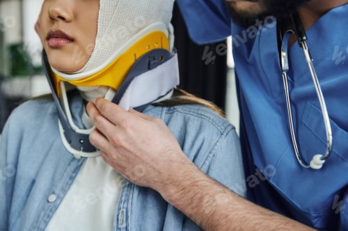 Preview: cropped view of professional medical instructor with stethoscope putting neck brace on young woman