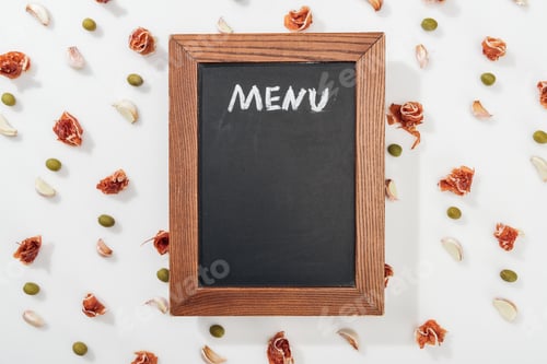 Preview: top view of chalk board with menu lettering among prosciutto, olives and garlic cloves