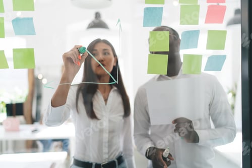 Preview: Multiethnic coworkers with highlighters standing at glass board in office