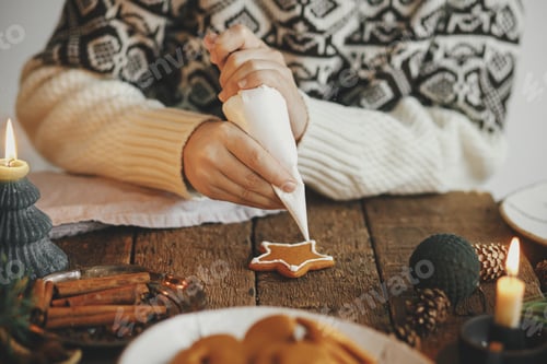 Preview: Hands decorating christmas gingerbread cookie star with icing on rustic table with decoration. Moody