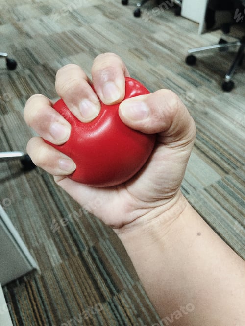 Preview: A hand squeezing a stress ball while inside the office to calm down.