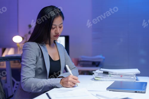 Preview: Young businesswoman sitting at her desk and signing documents, working late at night in a modern off