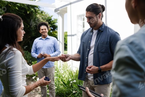 Preview: Exchanging rings outdoors, couple celebrating engagement with friends in garden