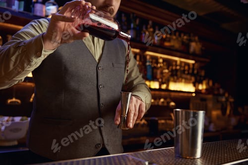 Preview: Bartender in uniform pouring drink into shaker behind bar