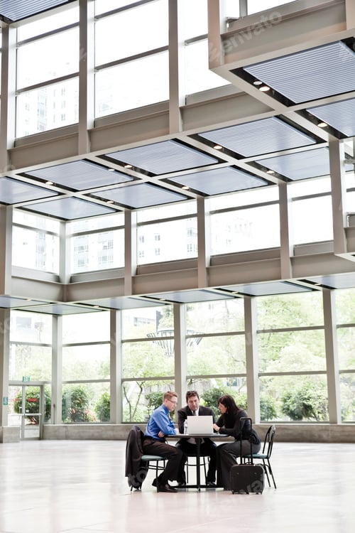 Preview: Three business people having a meeting at a table in a convention center lobby.