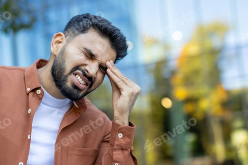 Preview: A man experiencing a headache, clutching his head in visible discomfort outdoors.