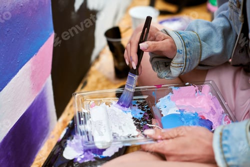 Preview: Female painter hand dips paintbrush into palette of colorful paints for live painting of picture