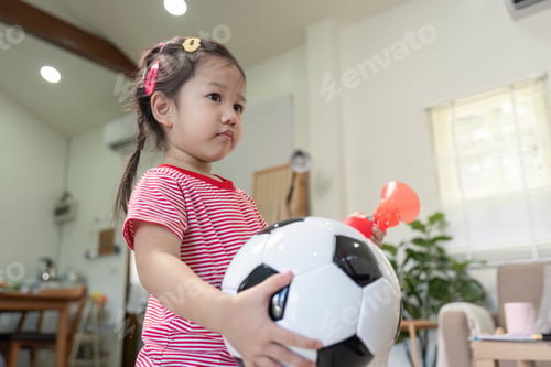 Preview: Young Asian girl holding a soccer ball in bright living room
