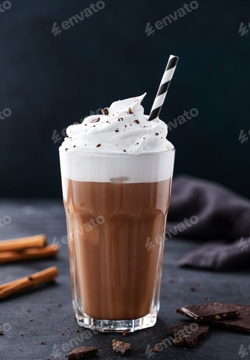 Preview: Hot chocolate with whipped cream, tube and cinnamon in a tall glass on a dark background. Front view
