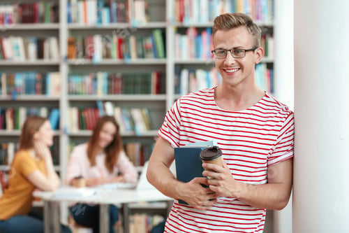 Preview: Young man with books and drink in library. Space for text