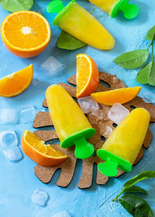 Preview: Homemade popsicles with orange juice, fruit ice on a blue stone or slate background. Copy space.
