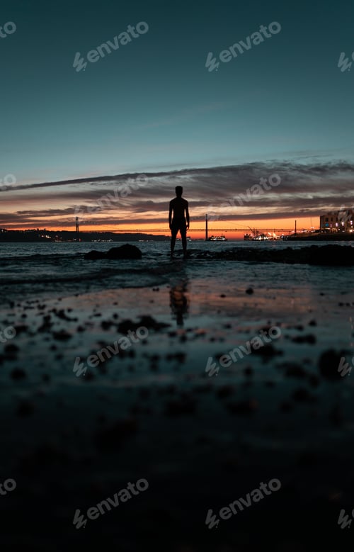 Preview: Silhouette of a young man watching the 25th of April Bridge sunset in Lisbon, Portugal