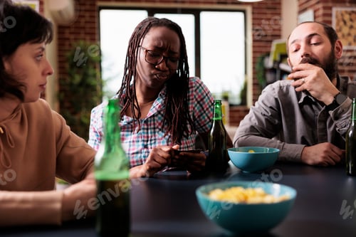 Preview: Casual multiethnic friends playing card games together while enjoying snacks and beverages.