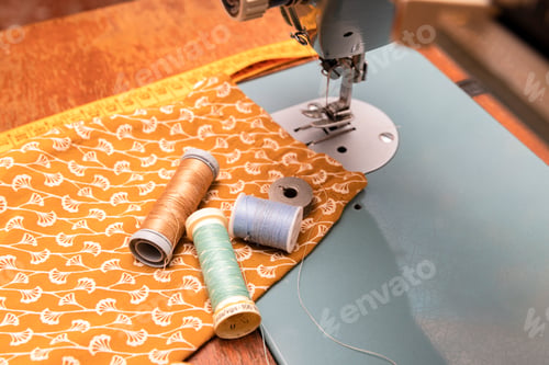 Preview: couturier material with foreground thread reels, tape measure, sewing machine and orange fabric