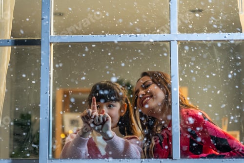 Preview: Adorable child looking at the window and admire snowflakes with mother.