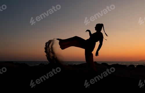 Preview: Silhouette of a woman dancing at a sandy beach at sunset. Caucasian woman posing outdoors at the