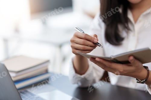 Preview: Close-up of a woman intently writing and taking notes in a notebook in the office.