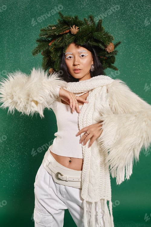 Preview: winter fashion, young woman with natural wreath posing in white stylish clothes under falling snow