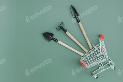 Preview: Three gardening tools and a shopping trolley on green.