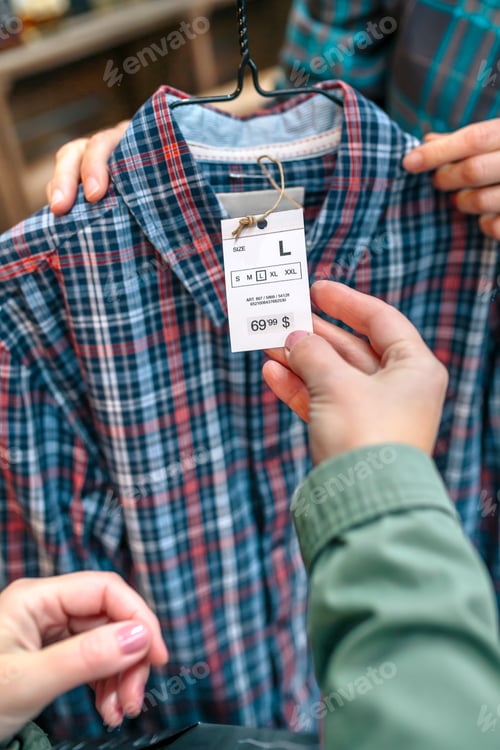 Preview: Close up of unrecognizable female customer hand holding label of plaid shirt on clothing store