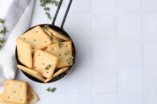 Preview: Tasty salty crackers and thyme on white tiled table, flat lay