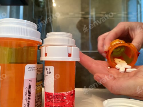 Preview: Woman’s hand pouring prescription drugs into her hand with more prescriptions in foreground