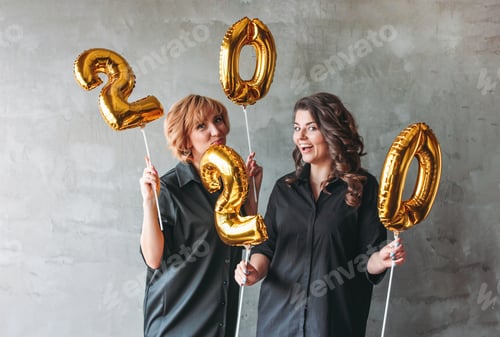 Preview: Two young women in black dresses holding the 2020 numbers balloons on the grey concrete wall
